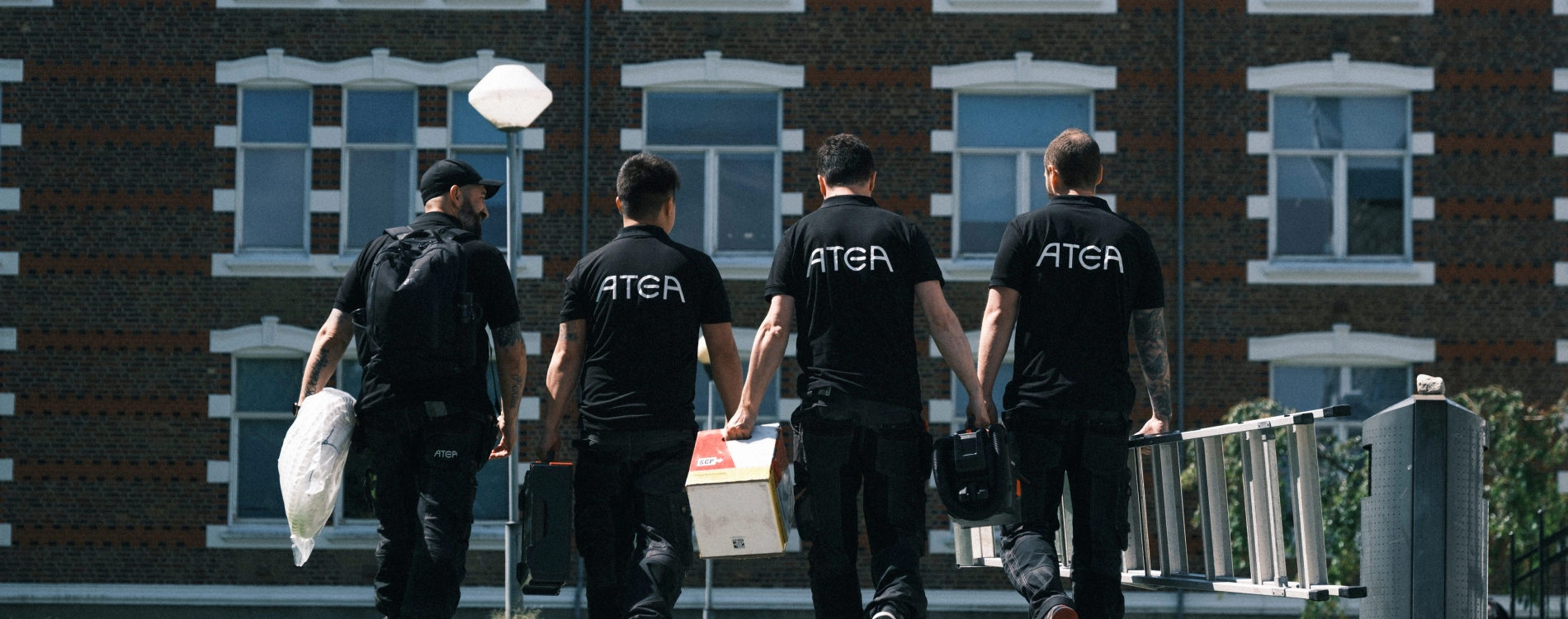 Four Men Wakling With Equipment In Black Atea Shirts