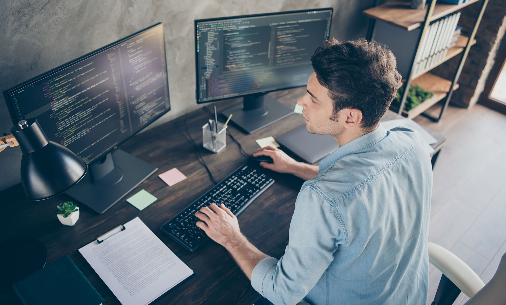 man sitting at desk and working on computer with two screens