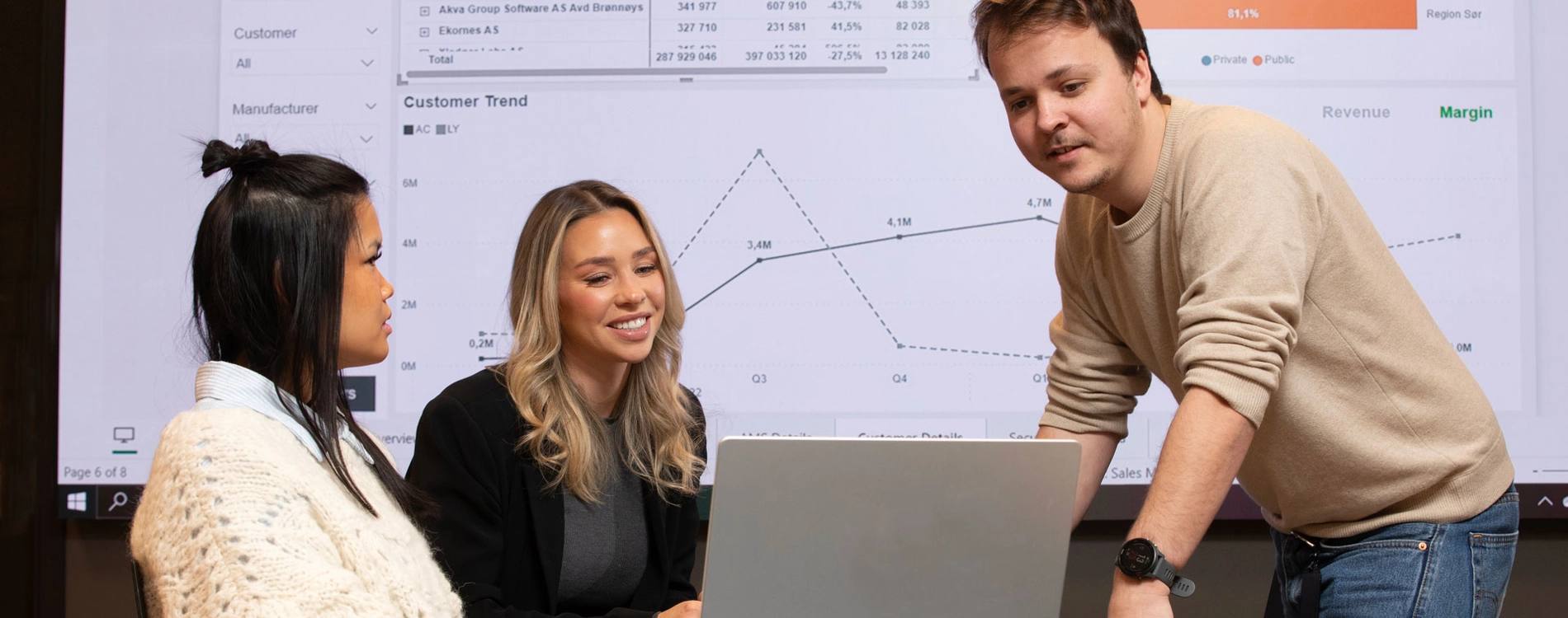 Three People Looking At Computer Screen In Front Of Big Screen