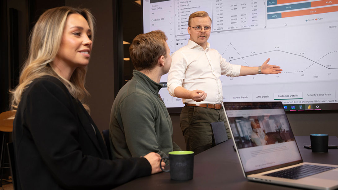 Three-people-in-meeting-with-screen-in-the-back-showing-numbers