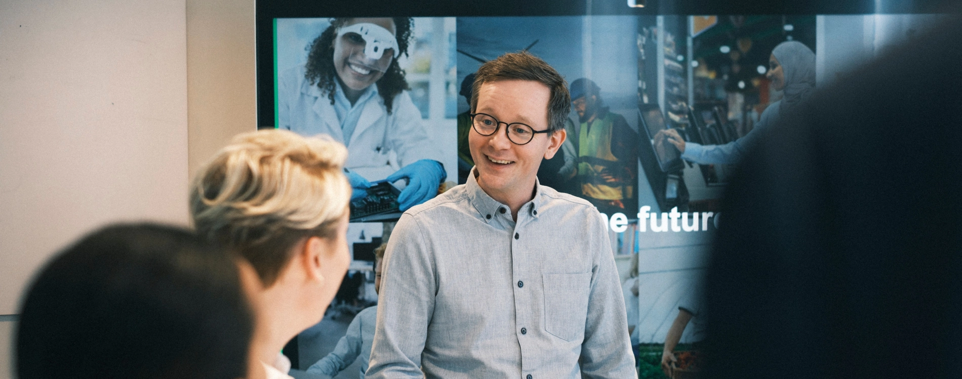 Man Presenting In Front Of Screen With Three People In The Meetingroom